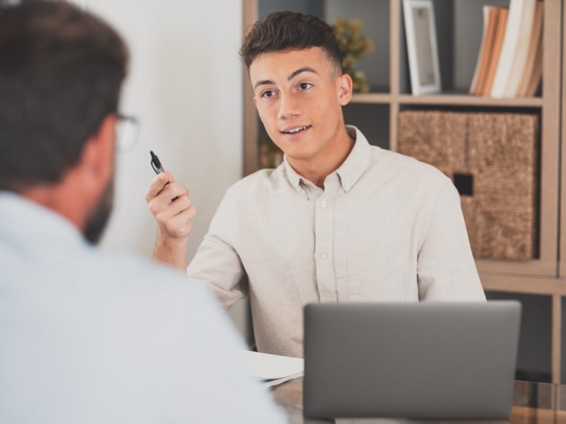 Portrait of teenager man smiling and talking to a man next to her talking about business work together in the office. Businessman working from home indoor.